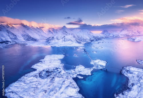 Aerial view of sea, snowy islands, mountains, road, violet sky at sunset in winter. Lofoten islands, Norway. Landscape with mountains and rocks in snow, water at dusk. Top view from drone. Nature