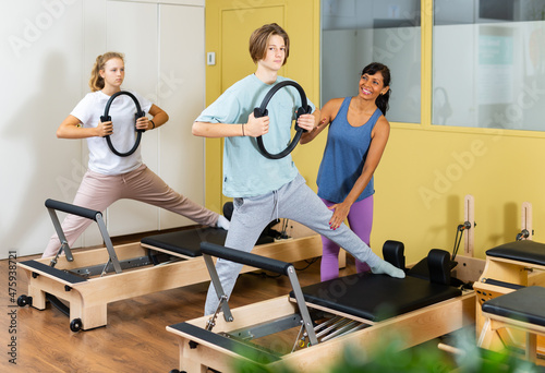 Teenager boy and girl exercising with pilates trainer latin woman in gym. They're training with pilates rings and reformers.