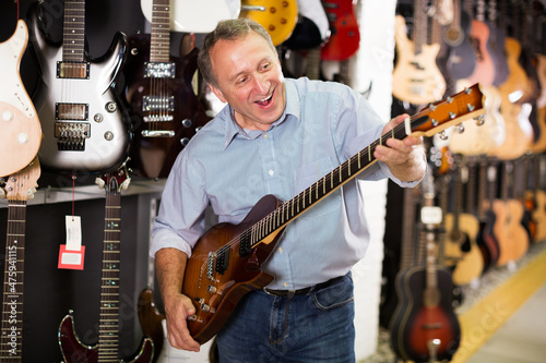 portrait of adult male is playing on electric guitar and satisfied it in music store.