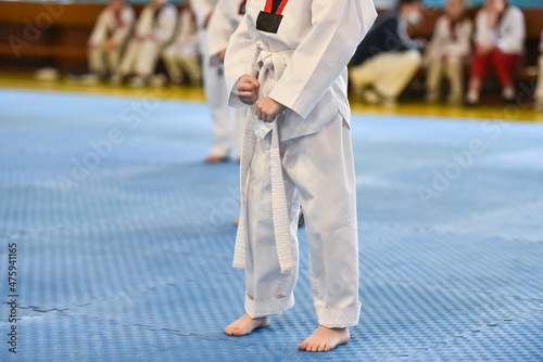 Taekwondo kids. A boy athlete stands in a taekwondo uniform with a white belt during a taekwondo tournament