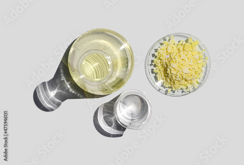 Closeup chemical ingredient on white laboratory table. Sodium sulfide flake in Chemical Watch Glass place next to Aluminium chloride liquid in Erlenmeyer flask. Top View