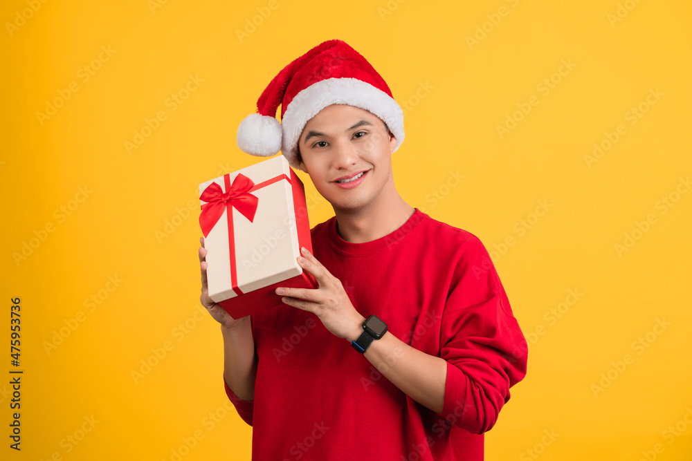 Happy smiling Asian young man holding gift box and looking at camera while enjoying yellow background. Happy smiling Asian young man holding gift box and looking at camera while enjoying yellow background.