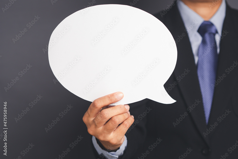 Businessman in suit holding an empty speech bubble standing against a gray background Businessman in suit holding an empty speech bubble standing against a gray background