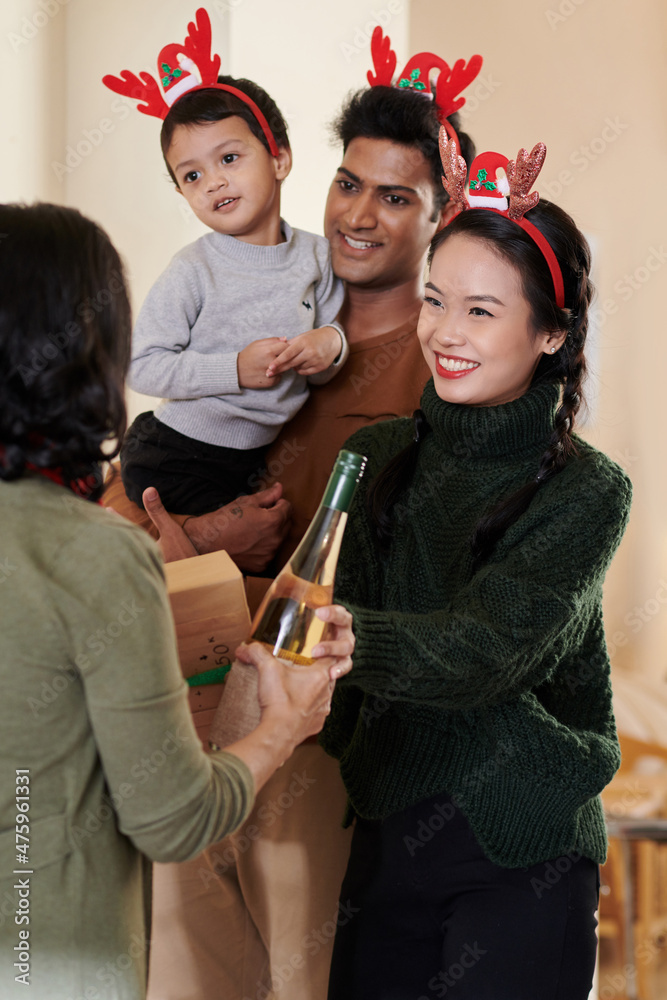 Fototapeta premium Cheerful young woman accepting present and wine her senior mother brought for Christmas
