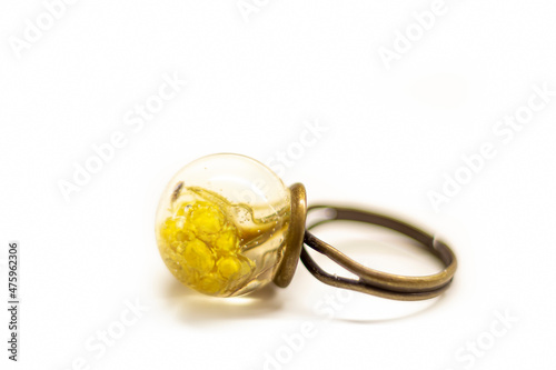 Handmade brass ring with flowers. Transparent epoxy resin ball with dried natural linden buds inside. Selective focus on the details, object isolated on white background. photo