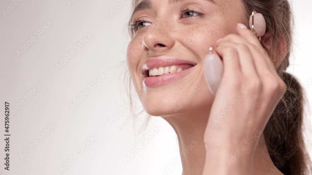 Close up portrait healthy young woman using jade facial roller for skin care, beauty treatment on white isolate background. Brunette female using natural massager. Face massage. Close up portrait healthy young woman using jade facial roller for skin care, beauty treatment on white isolate background. Brunette female using natural massager. Face massage.