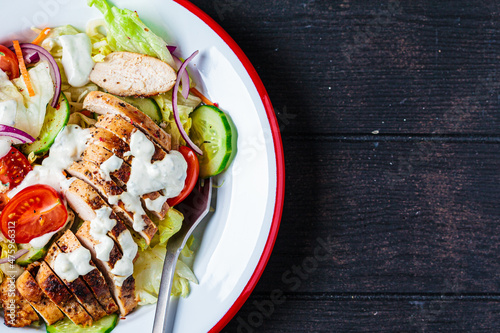 Buffalo chicken salad with gorgonzola cheese, tomato, cucumber and ranch dressing, dark wooden background.
