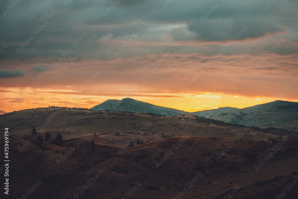Atmospheric landscape with silhouettes of mountains with trees on background of orange dawn sky. Colorful nature scenery with sunset or sunrise. Sundown paysage in vintage colors and faded tones.