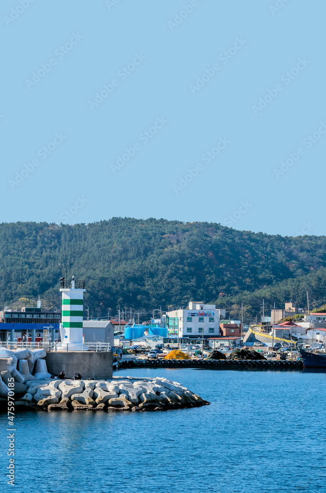 Landscape of small seaport with green and white lighthouse on pier.