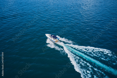 Large white yacht movement on the water diagonally top view. White boat with blue awning moves in the sea aerial view.