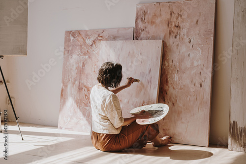 Young woman artist painting abstract picture in studio with sun light. Aesthetic minimalist art work creation concept photo