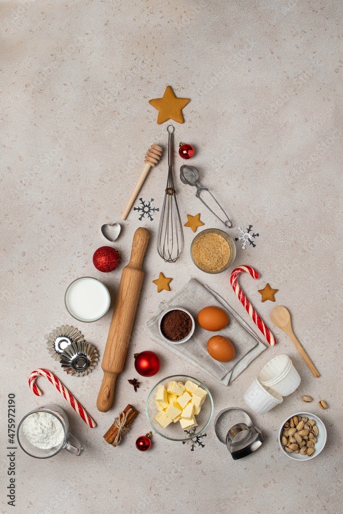 Christmas or New Year baking background. Abstract christmas tree made from baking tools and food ingredients for baking - flour, eggs, sugar, milk, nuts on beige background. Copy space, top view.
