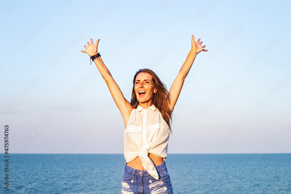 Smiling young woman with raised hands on the background of the sea. Smiling young woman with raised hands on the background of the sea.