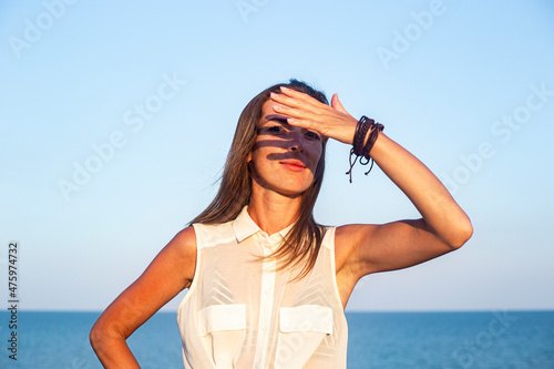 Young woman covers her face from the sun with her palm against the background of the sea.