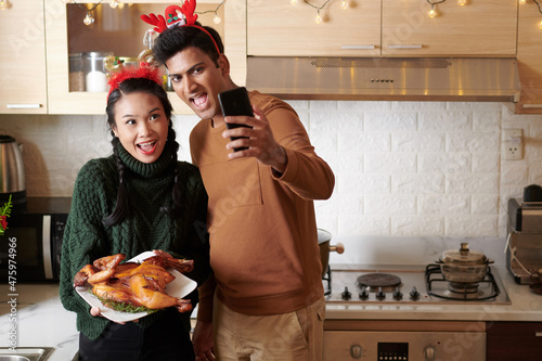 Excited joyful young couple video calling friends or family memebers and showing grilled chicken for Christmas dinner photo