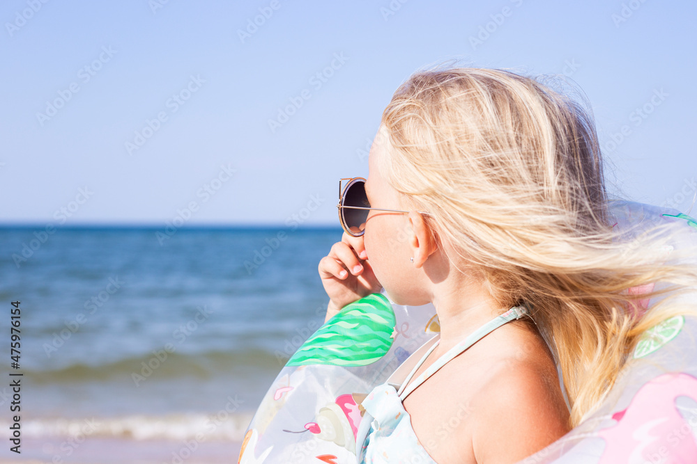 Child girl with sunglasses with a rubber ring on the beach.