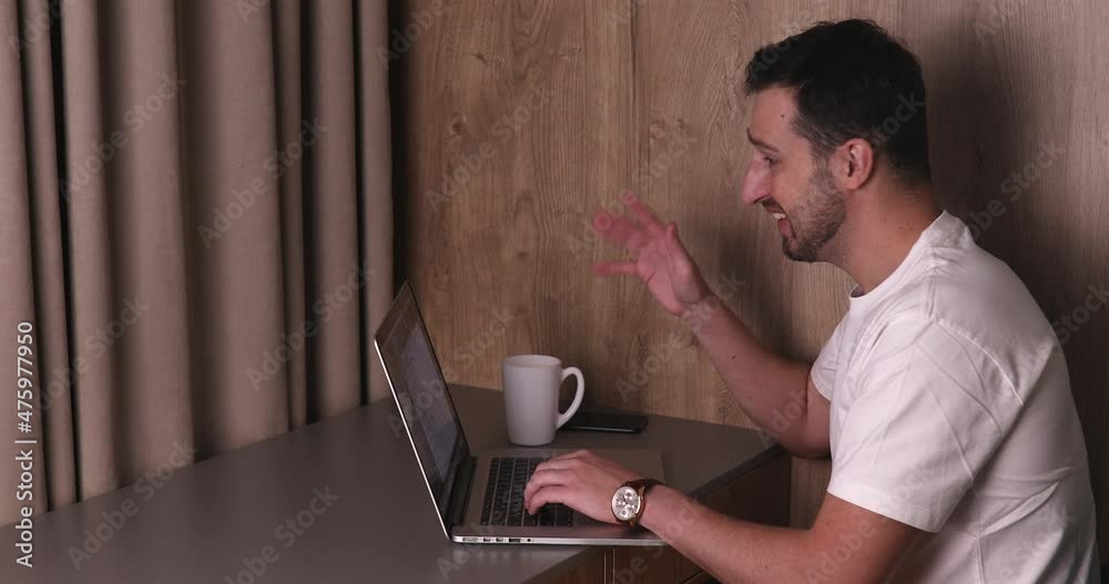 Smiling young adult man vlogger look at camera talk make live video conference call online chat using computer at home. Smiling young adult man vlogger look at camera talk make live video conference call online chat using computer at home.