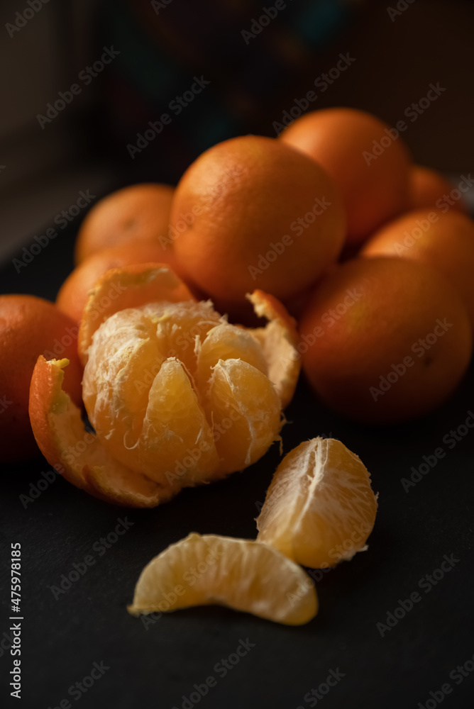 Peeled slices and half-peeled tangerine on dark surface close up Peeled slices and half-peeled tangerine on dark surface close up