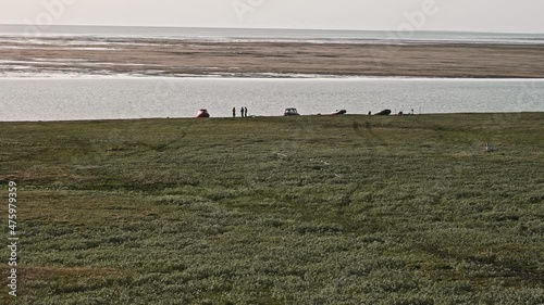 Faraway view of people silhouettes standing and walking near boats that are near the river on shore. Research in Yamal Peninsula. photo