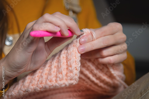 A young Caucasian woman in casual home clothes knits a pink wool hat or scarf. A useful hobby is home production of clothes. Close-up