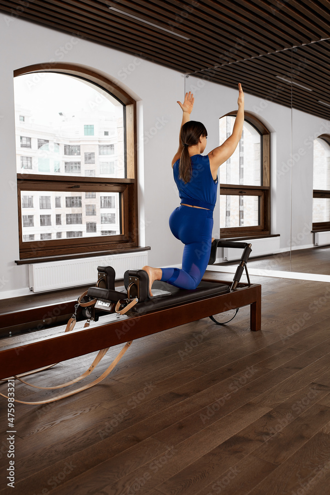 Young girl doing pilates exercises with a reformer bed. Beautiful slim fitness trainer on reformer. Fitness concept