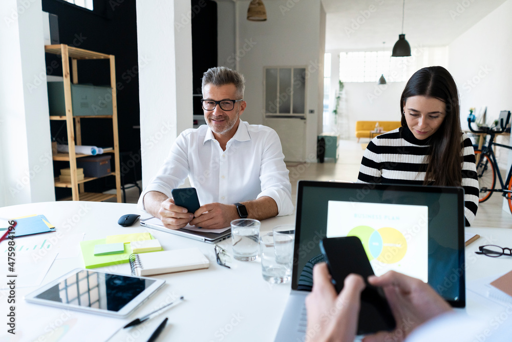 Businessman with smart phone sitting with colleagues working at office Businessman with smart phone sitting with colleagues working at office