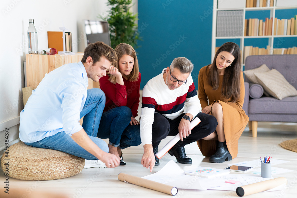 Businessman pointing at documents with colleagues crouching on floor in office Businessman pointing at documents with colleagues crouching on floor in office