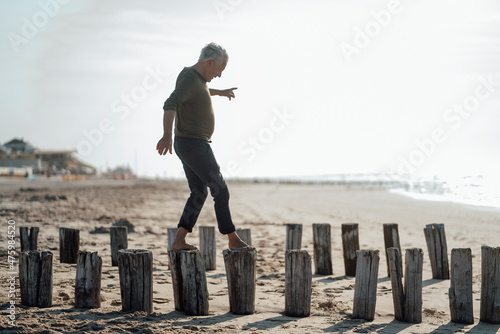 Senior man balancing on wooden posts at beach photo