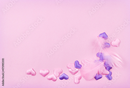 Feathers and pink and purple satin hearts in a cornar arrangement on paper texture for Valentine Day