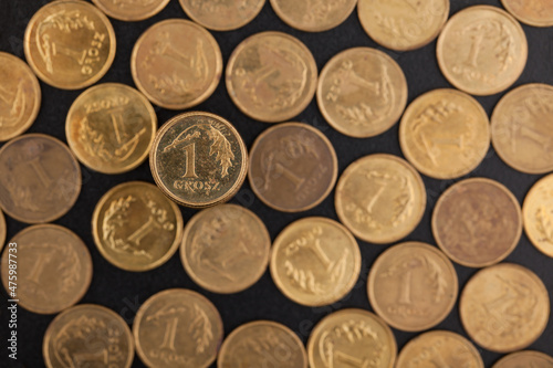 In the foreground a one penny coin, in the background blurred coins lying on a dark background.