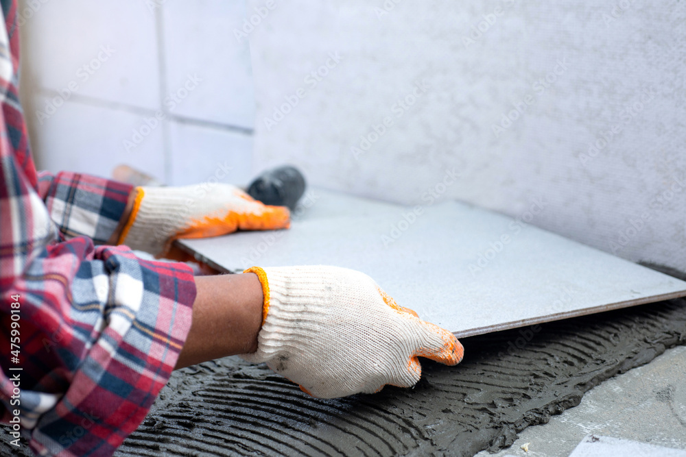 Hands of man  is laying ceramic tiles on the floor, home repair by yourself, selective focus