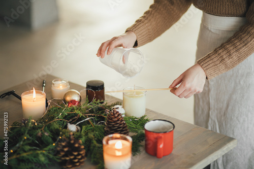 Woman making candle of soy wax, using wooden stick.