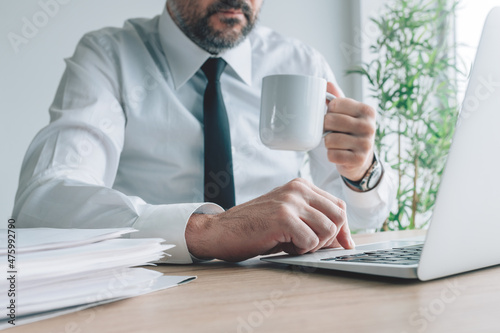 Drinking coffee at the office, businessman with coffee cup and laptop at his workplace