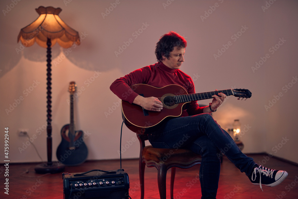 Obraz premium Male musician playing acoustic guitar on the amplifier in retro vintage room.