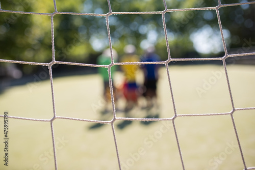 Close-up of football net on summer day. Blurry senior men standing on field in background. Football, sport, leisure concept