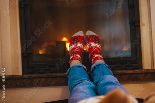 Feet of unrecognizable woman in woollen socks by the Christmas fireplace. Winter and Christmas holidays concept. Woman in Christmas mood. Young woman in her home in Christmas time