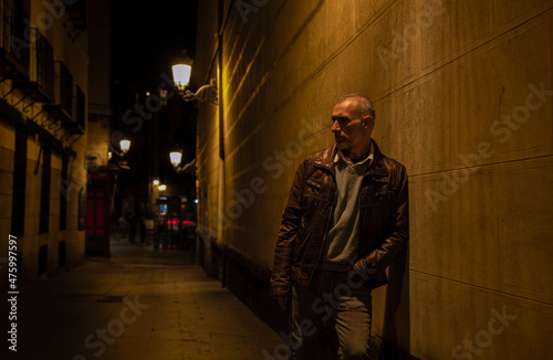 Adult man on street against brick wall with light of street lamp at night. Shot in Madrid, Spain