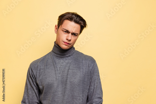 Studio shot of young handsome displeased man, student wearing warm gray polo-neck isolated on yellow studio background. © master1305
