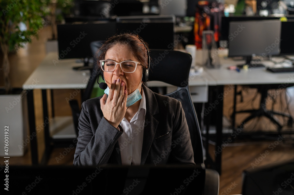 Business woman in a medical mask yawns at her desk in the office. Business woman in a medical mask yawns at her desk in the office.