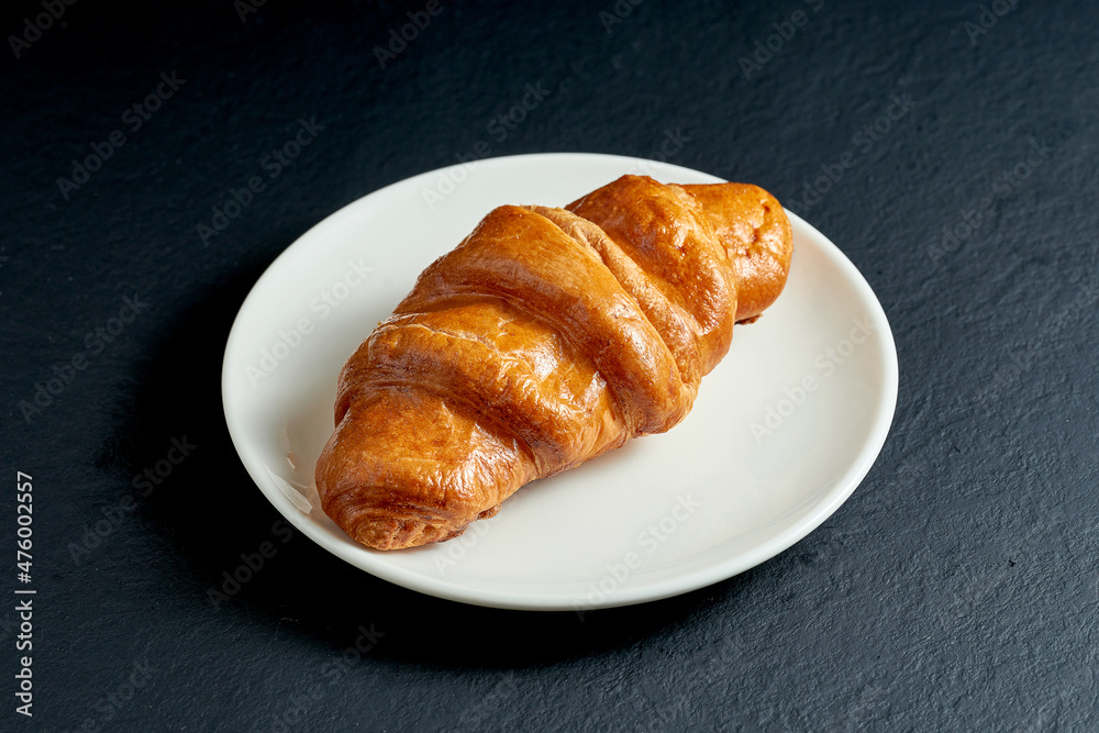 Creamy sweet croissant in white plate on black background
