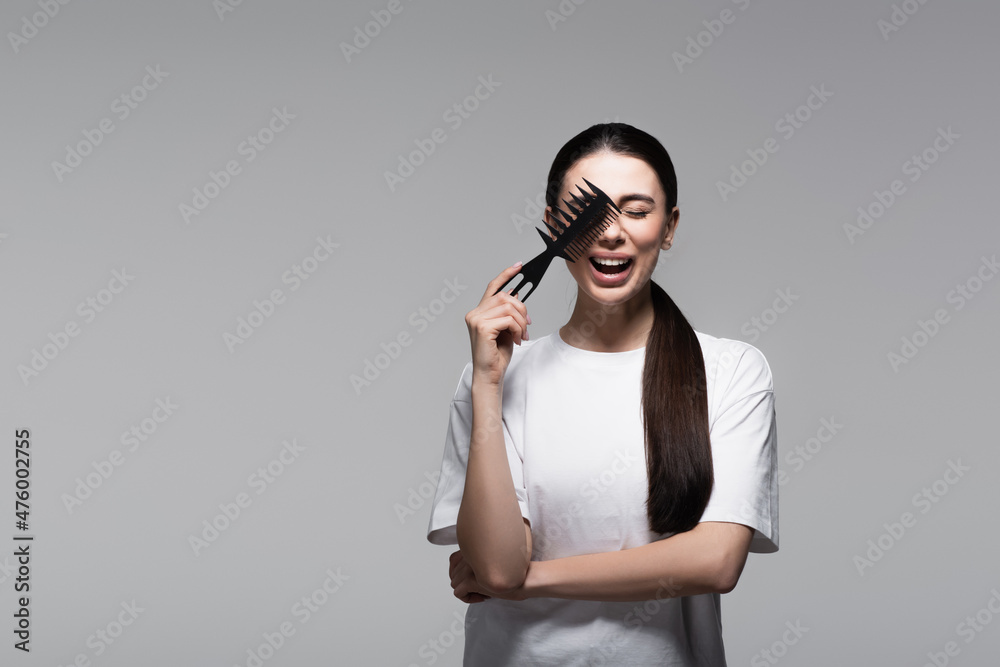 Obraz premium positive woman in white t-shirt holding comb near straight hair isolated on grey