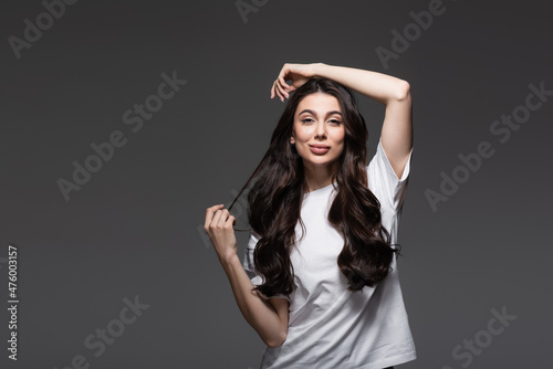 young pleased woman with wavy hair looking at camera on dark grey