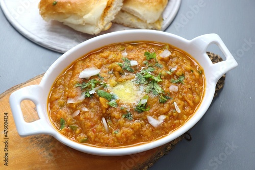 Indian Mumbai Street style Pav Bhaji, garnished with peas, raw onions, coriander, and Butter. Spicy thick curry made of out mixed vegetables served with pav over black background with copy space.