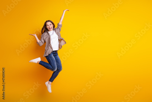 Full size profile side photo of young cheerful girl jump advertise advantage solution isolated over yellow color background photo