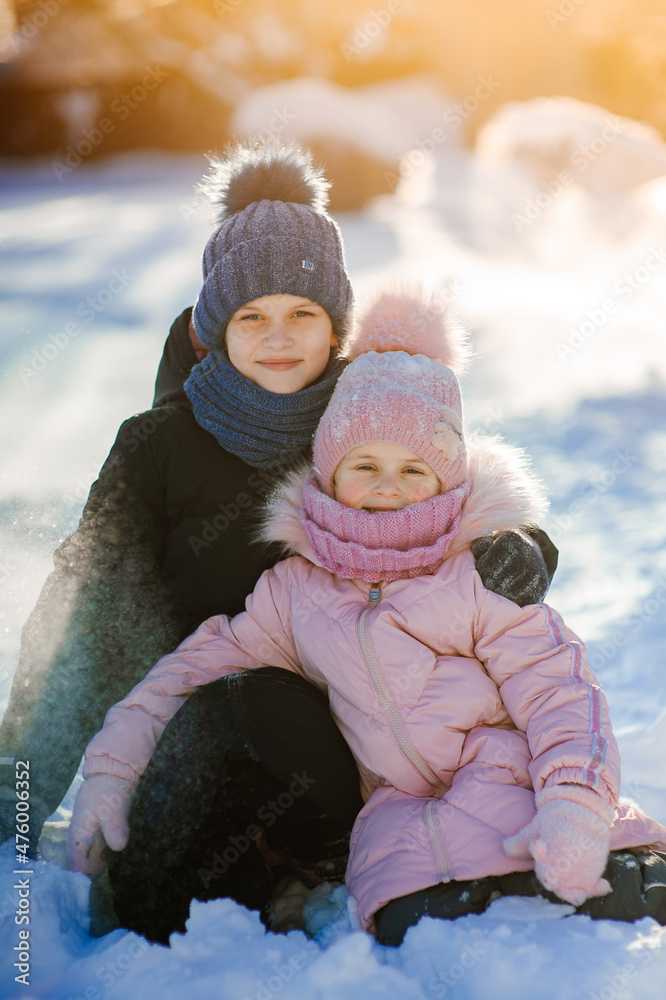 Two cute girls, the youngest and the oldest, are sitting in a winter park and playing with snow. Family values. Winter fun