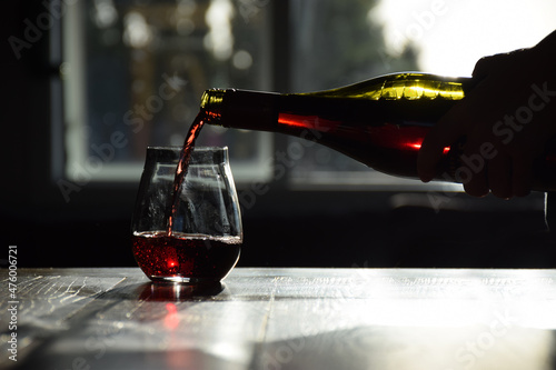 A fine red wine is poured into a stemless glass from a bottle photo