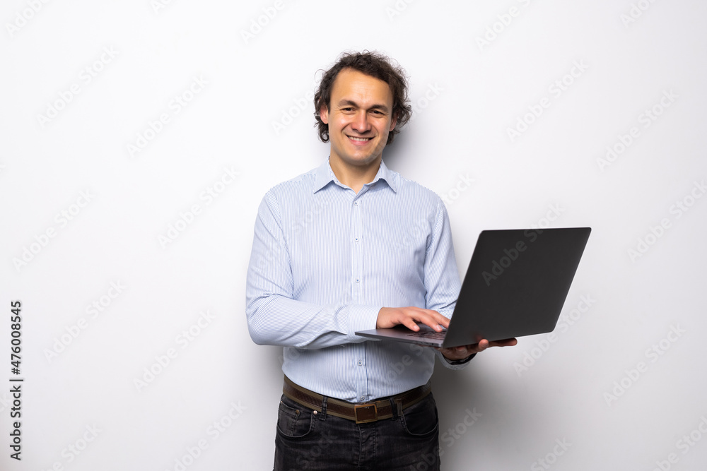 Confident young man holding laptop and smiling while standing against white background