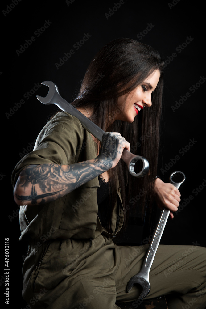 Atrakcyjna uśmiechnięta dziewczyna - mechanik z tatuażami, pozująca z dwoma bardzo dużymi kluczami. Zdjęcie studyjne na białym tle, oświetlenie z 2 lamp. - obrazy, fototapety, plakaty 