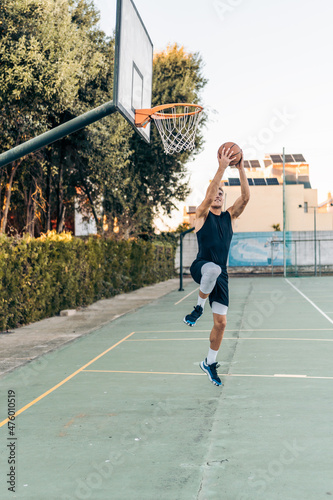 Vertical photo of a tall caucasian man jumping while shooting a ball in a basket