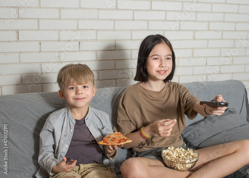 a boy and a girl are sitting on the couch, watching TV, eating homemade pizza and popcorn. the concept of brother and sister communication.